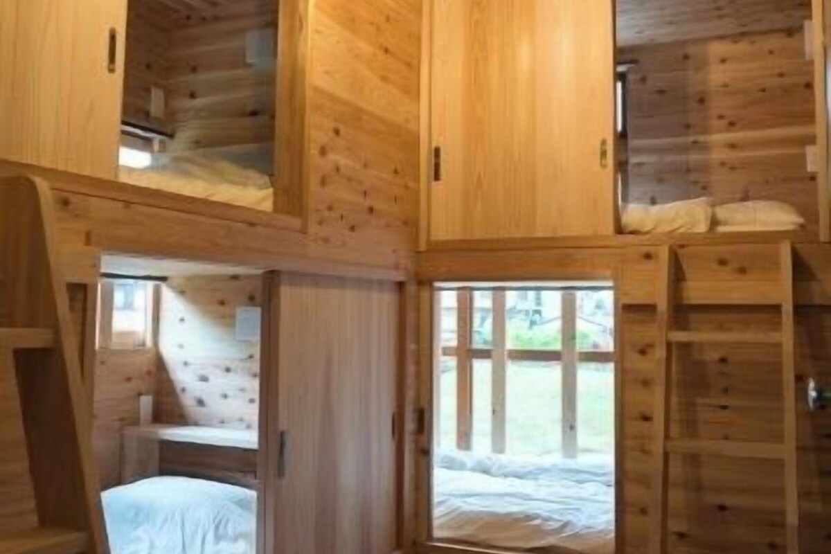 A wooden cabin interior with a loft bed, a ladder, and a window.