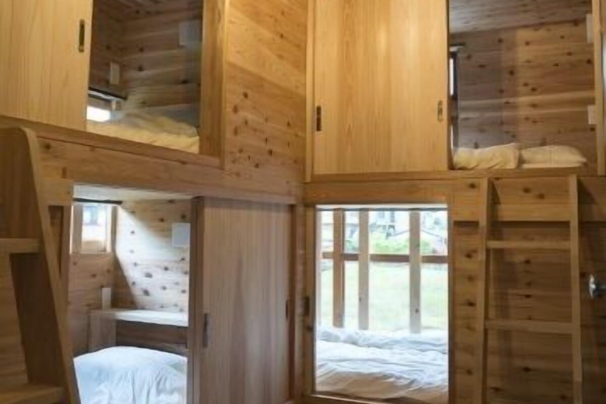 A wooden cabin interior with a loft bed, a ladder, and a window.