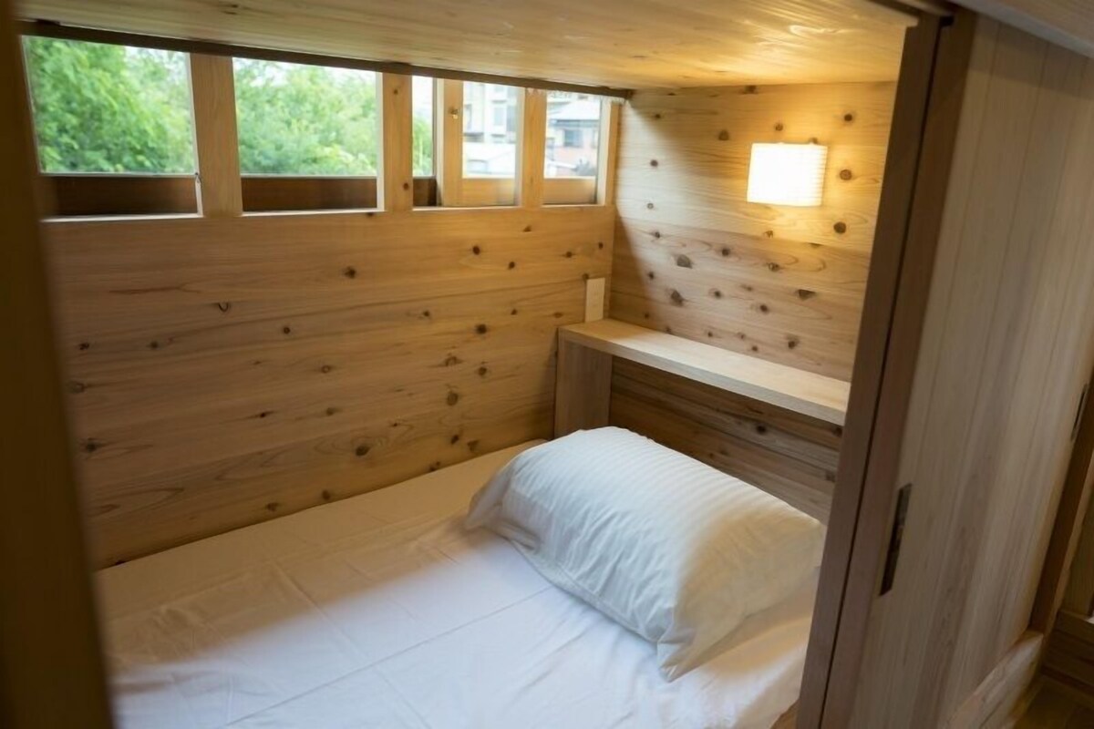 A small wooden room with a bed, a bench, and a window.