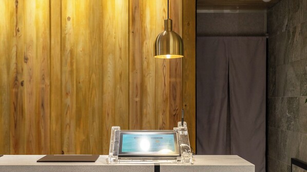 Un mur en bois, une suspension lumineuse, une tablette posée sur un support et un mur en pierre.