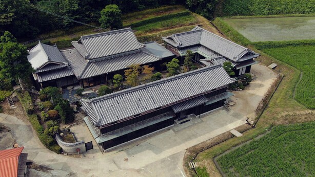 Un edificio japonés tradicional con varias construcciones, rodeado de follaje y campos.