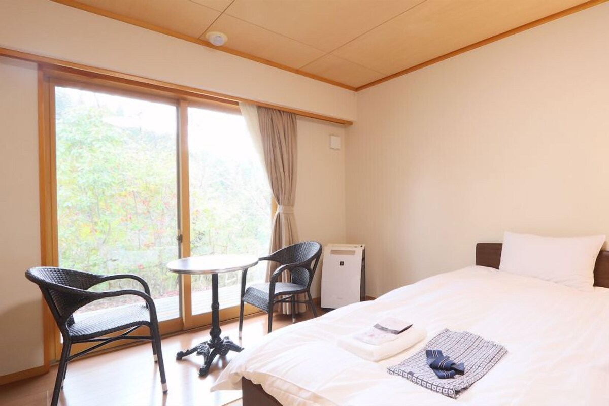 Een hotelkamer met een bed, een bureau, twee stoelen, een tafel, een lamp en een wekker.