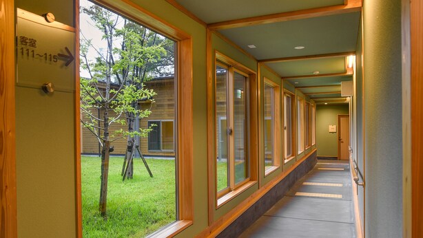 A corridor with large windows, a sign indicating room numbers 111-115, and a tree outside. - Hanazono Onsen Kaho no Sato (Katsuragi)