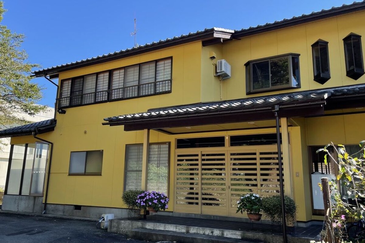 Un edificio de dos pisos con fachada amarilla, un acceso cubierto y una puerta de garaje.