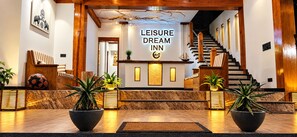 Un vestíbulo de hotel con una escalera, una mesa de recepción y plantas en macetas.