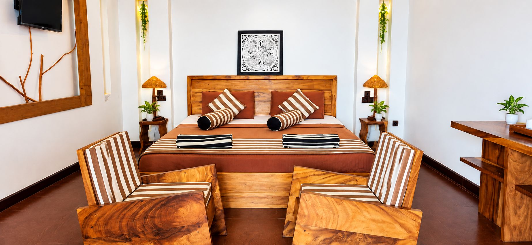 A hotel room with a wooden bed, striped pillows, a wooden bench, and a desk.