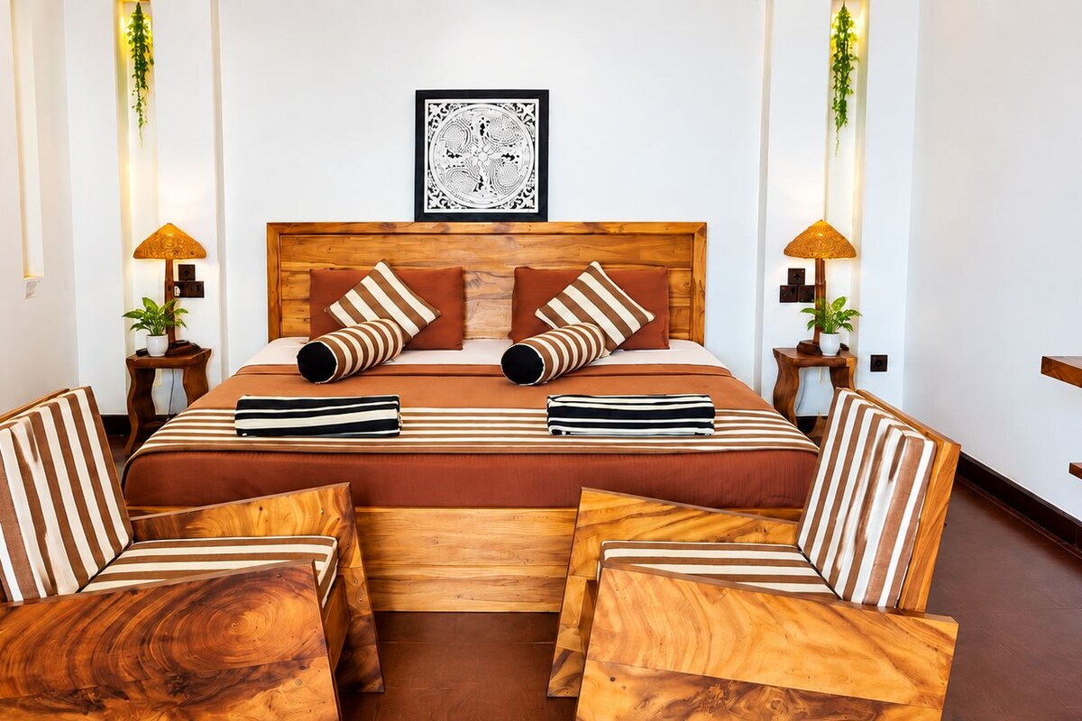 A hotel room with a wooden bed, striped pillows, a wooden bench, and a desk.