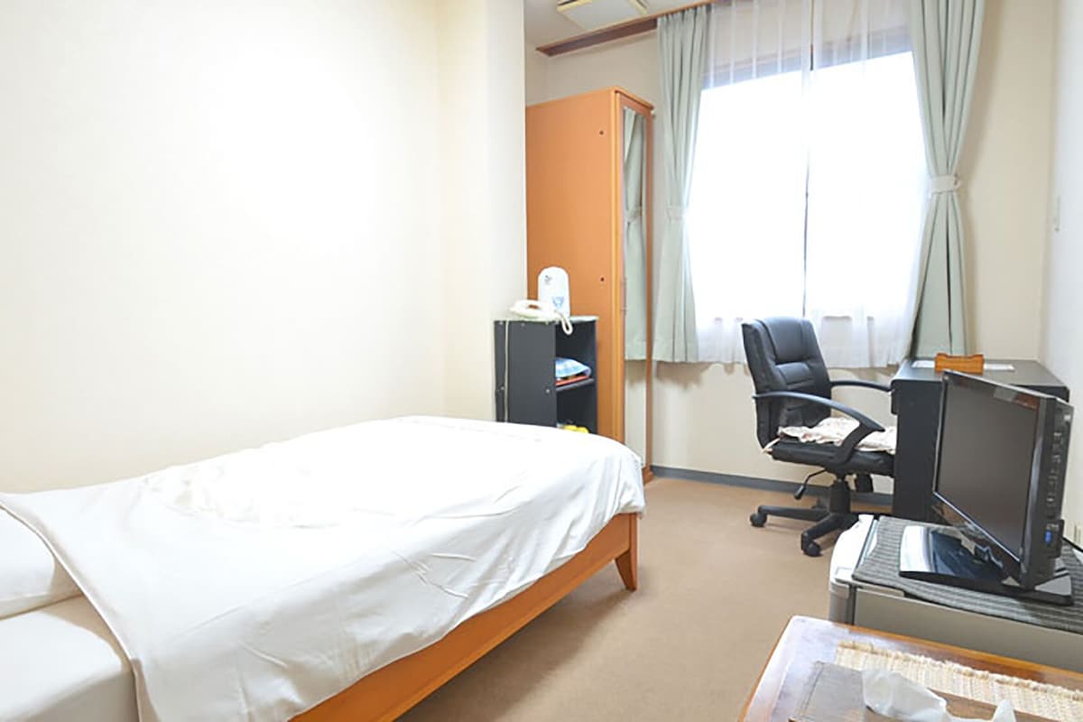 A hotel room with a single bed, a desk with a computer, a chair, and a wardrobe.