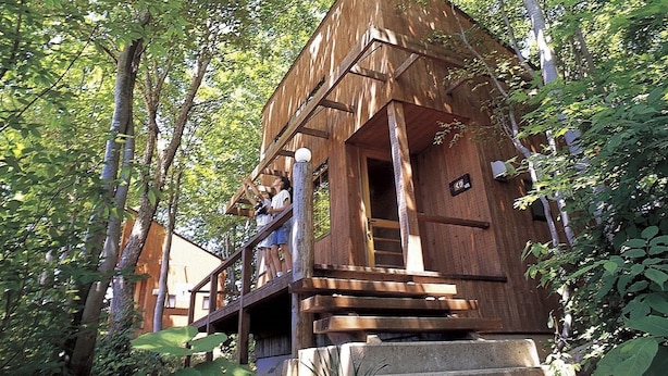 Una cabaña de madera con balcón, rodeada de árboles.