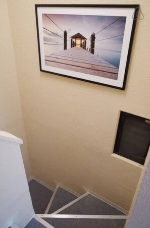 A framed picture of a pier with a small building at the end, mounted on a beige wall. - Tora Hotel Kitaueno (Tokyo)