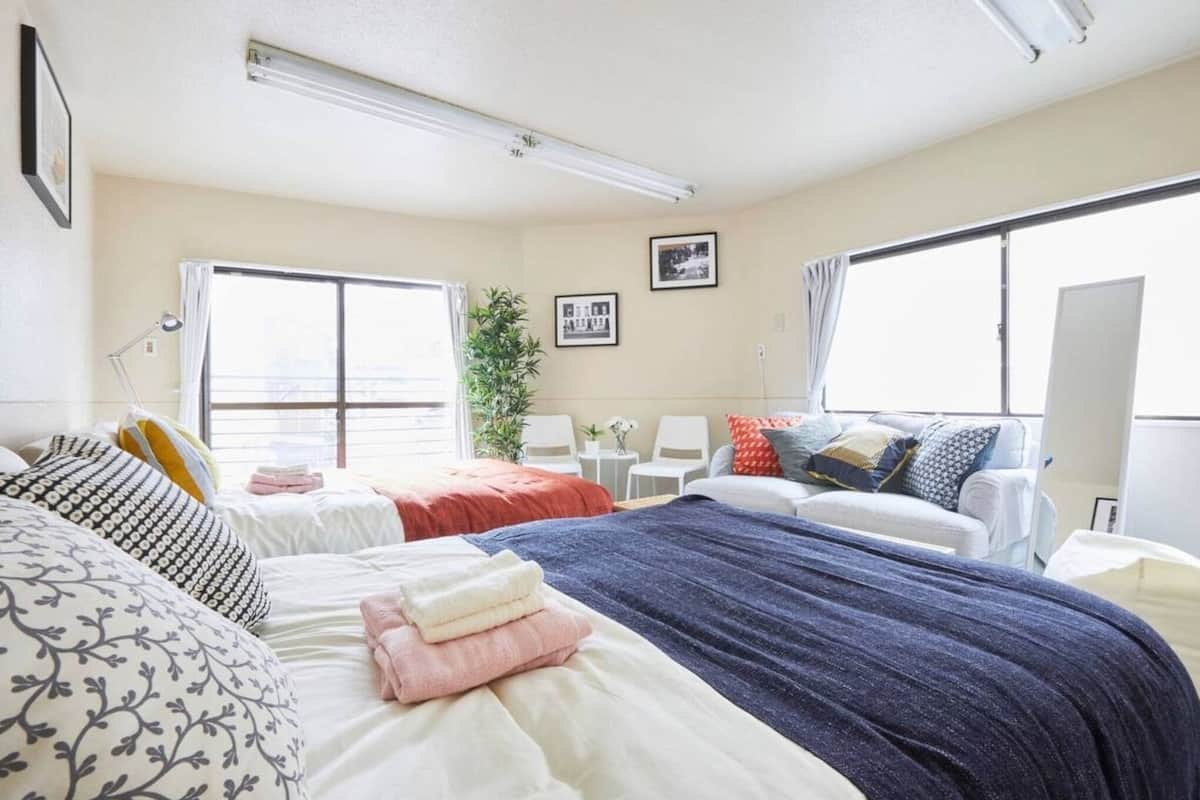 Hotellihuone, jossa on kaksi sänkyä, suuri ikkuna, viherkasvi ja työpöytä tuolilla.
