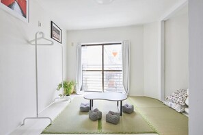 A room with a tatami mat floor, a low table, a hanging coat rack, a potted plant, and a window with curtains. - Tora Hotel Kitaueno (Tokyo)