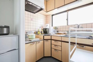 A compact kitchen with a refrigerator, stove, and sink. - Tora Hotel Kitaueno (Tokyo)