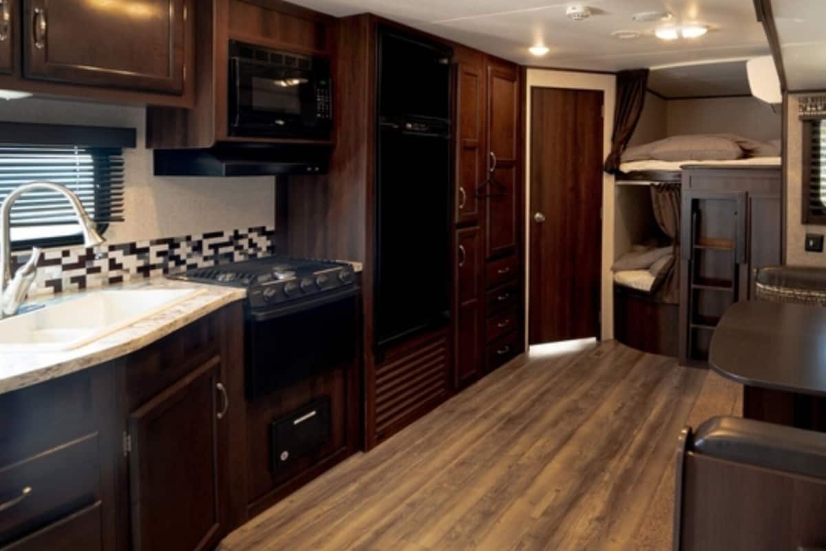 A compact RV kitchen with a stove, microwave, and sink.