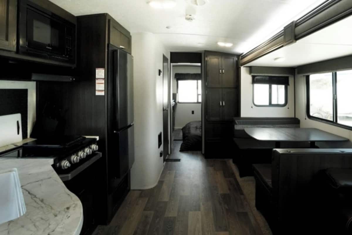 A compact RV interior with a kitchen area, a dining space, and a seating area with a window.