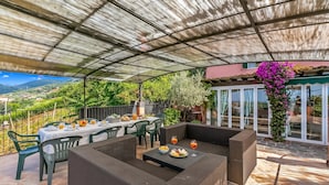 Eine Terrasse im Freien mit überdachter Sitzgruppe, Esstischen und Blick auf die Landschaft.