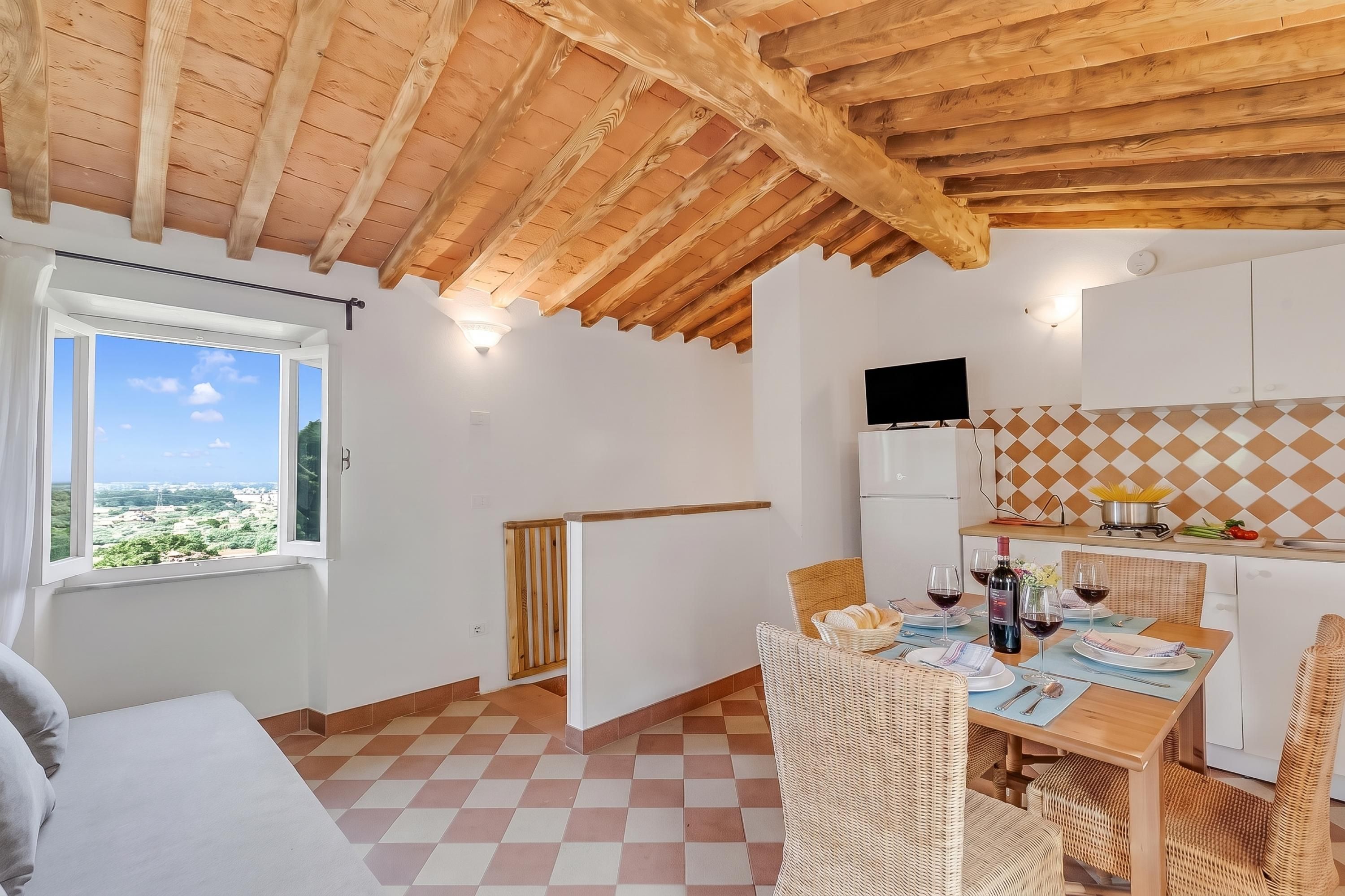 Ein Zimmer mit Holzboden, einem Fenster mit Aussicht, einer Essecke mit Tisch für zwei Personen und einer Küche mit gefliestem Rücksprung.