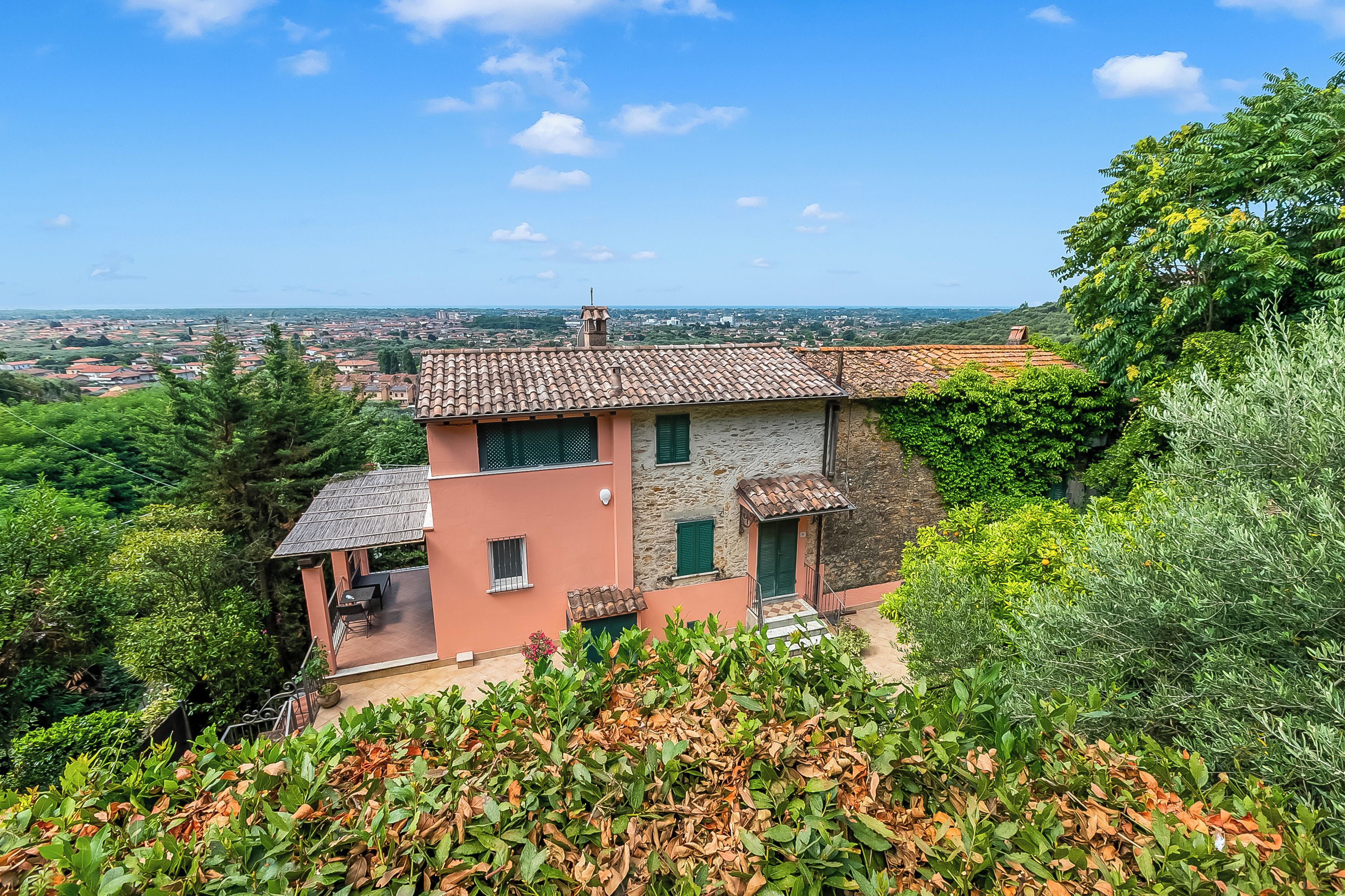 A hillside villa with a stone facade, a terrace, and a view of the surrounding landscape.