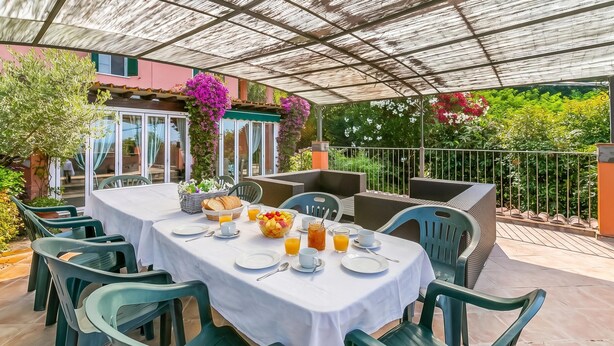 Ein Essbereich im Freien mit einer überdachten Terrasse, Tische gedeckt mit Tellern, Tassen und einer Obstschale.