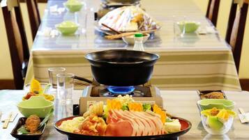 Een eettafel met verschillende gerechten, een zwarte pan op een gasbrander en groene kommen.