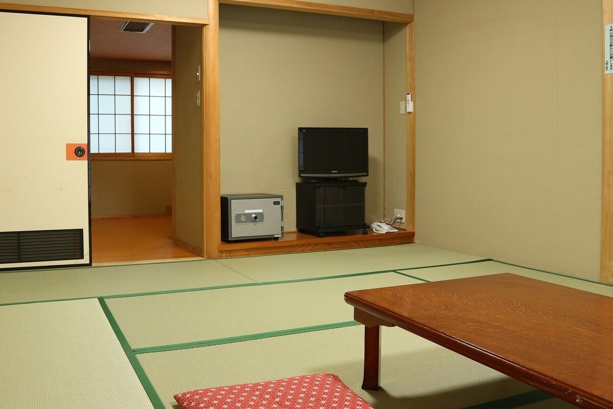 Een traditionele Japanse kamer met tatami vloerbedekking, een houten tafel, een televisie en een kluisje.