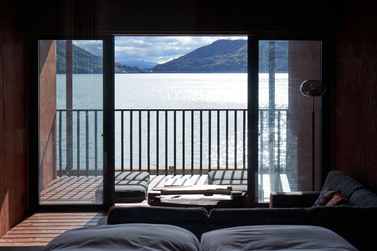Une pièce dotée d’une grande porte-fenêtre coulissante donnant sur un balcon avec vue sur un lac et des montagnes.
