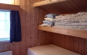 L’intérieur d’une cabane en bois, avec un lit superposé, une fenêtre avec des rideaux et un radiateur.