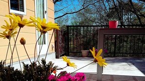 Une plante en pot, ornée de fleurs jaunes et roses, se trouve devant un immeuble doté d’un balcon.