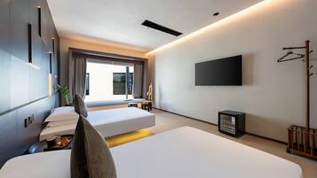 A modern hotel room with two beds, a flat-screen TV, a coat rack, and a small table with a plant.