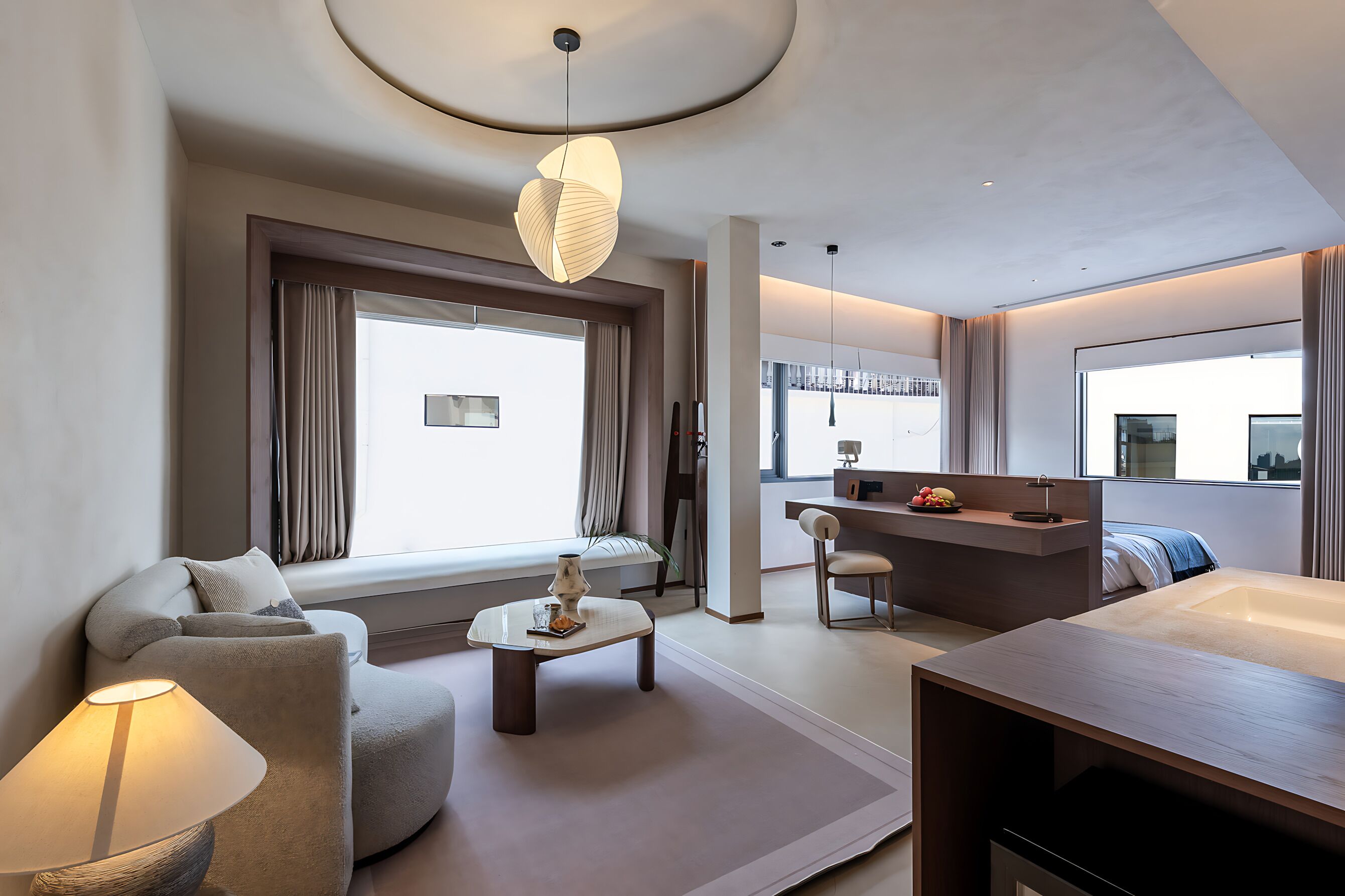 Et moderne hotelværelse med sofa, lille sofabord, skrivebord, stort vindue, badeværelse og byudsigt.