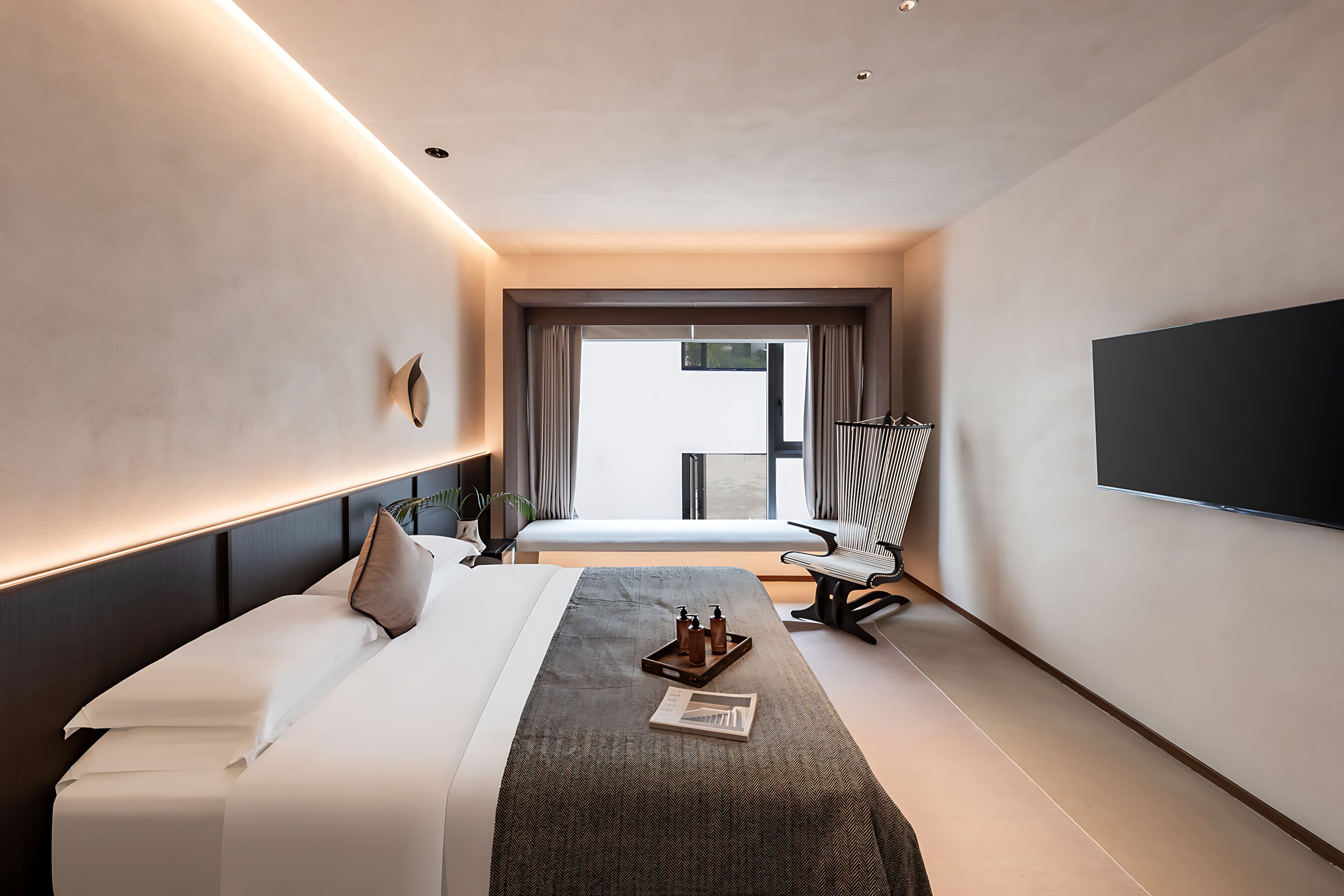 Een moderne hotelkamer met een groot bed, een flatscreen-televisie, een zithoek met een fauteuil, en een raam met uitzicht.