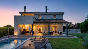 Una casa moderna con piscina, mobiliario de exterior y un patio bien iluminado.