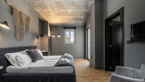 Habitación de hotel moderna con una cama grande, zona de estar, un tapiz macramé en la pared y una ventana que proporciona luz natural.