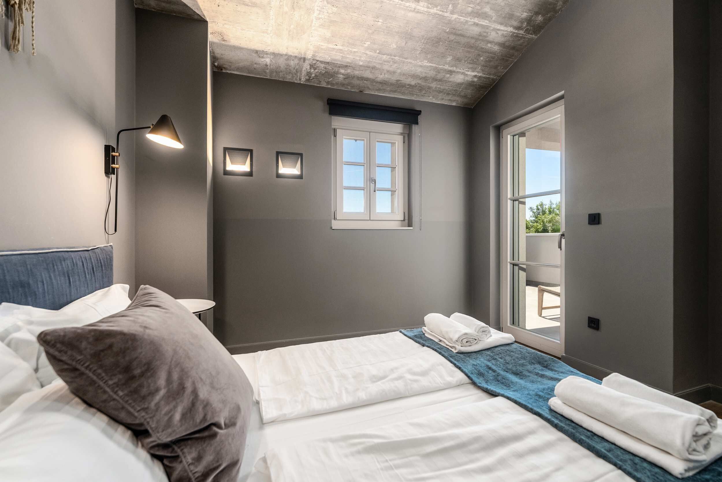 Habitació d'hotel amb un llit, una tauleta de nit, una làmpada penjada a la paret, una finestra i vista a l'exterior.