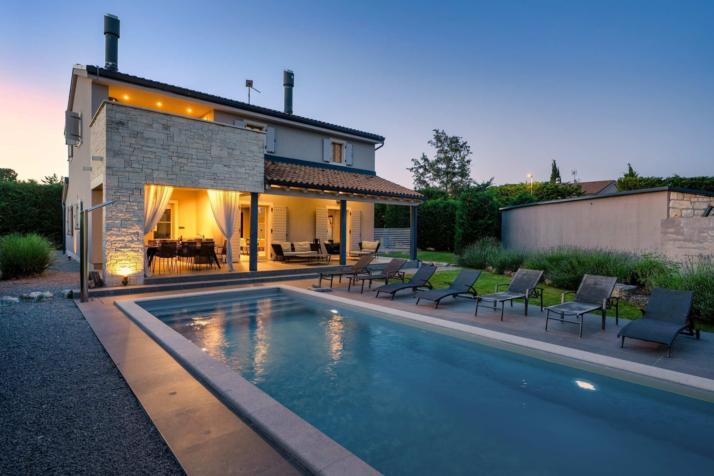A modern house with a swimming pool, outdoor seating, and a stone facade.