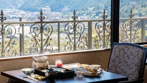 A dining table with various dishes, a bowl, and a teapot, set against a view of a cityscape and mountains through a balcony railing. - Hotel de Marronnier Gero Onsen (Gero)
