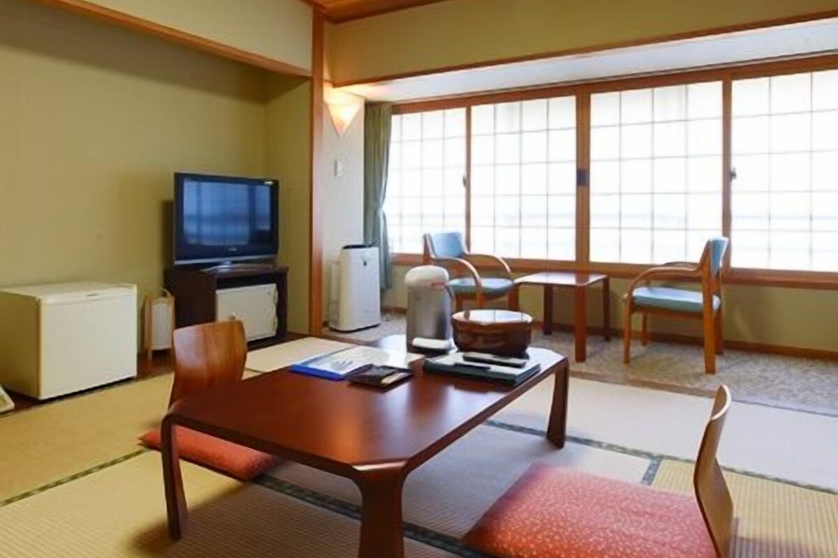 A traditional Japanese-style room with tatami flooring, a low table, chairs, a television, and a sliding door.