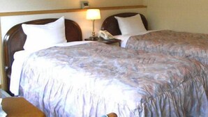 Una habitació d'hotel amb dos llits, una tauleta de nit amb una làmpada i un panell de fusta al capçal.