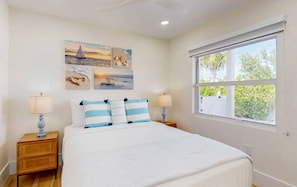 A bedroom with a bed, two nightstands, a window, and wall art. - Luxury Oceanfront Estate | Private Dock • Pool (Key Largo)