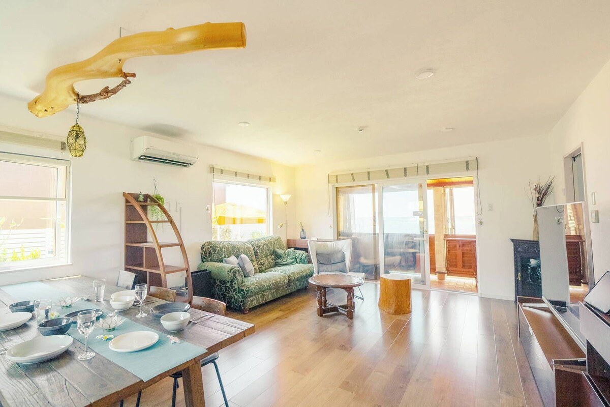 A spacious living area with a dining table set for four, a sofa, and a balcony with a view.