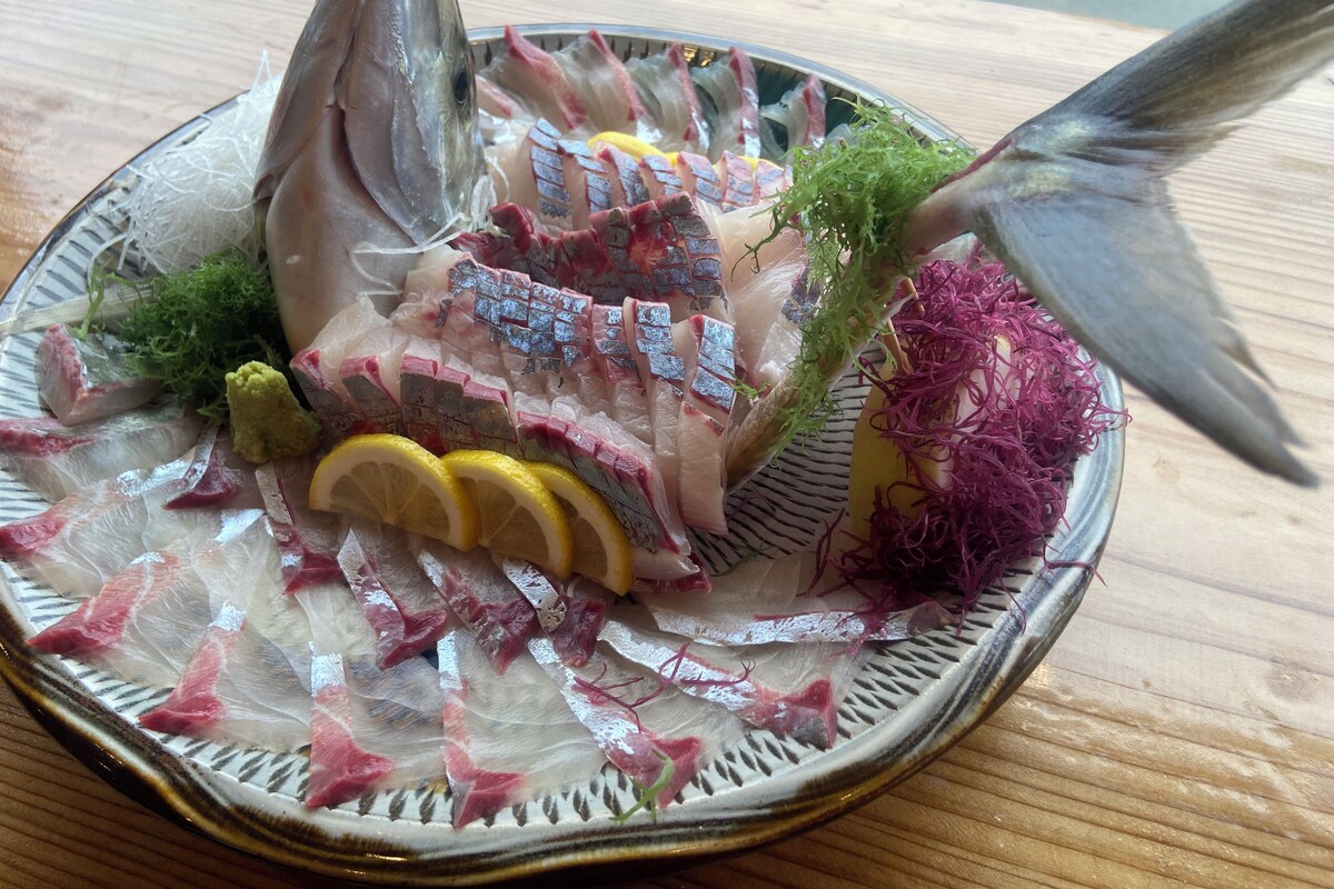 A plate of sashimi with various fish slices, garnishes, and a whole fish.