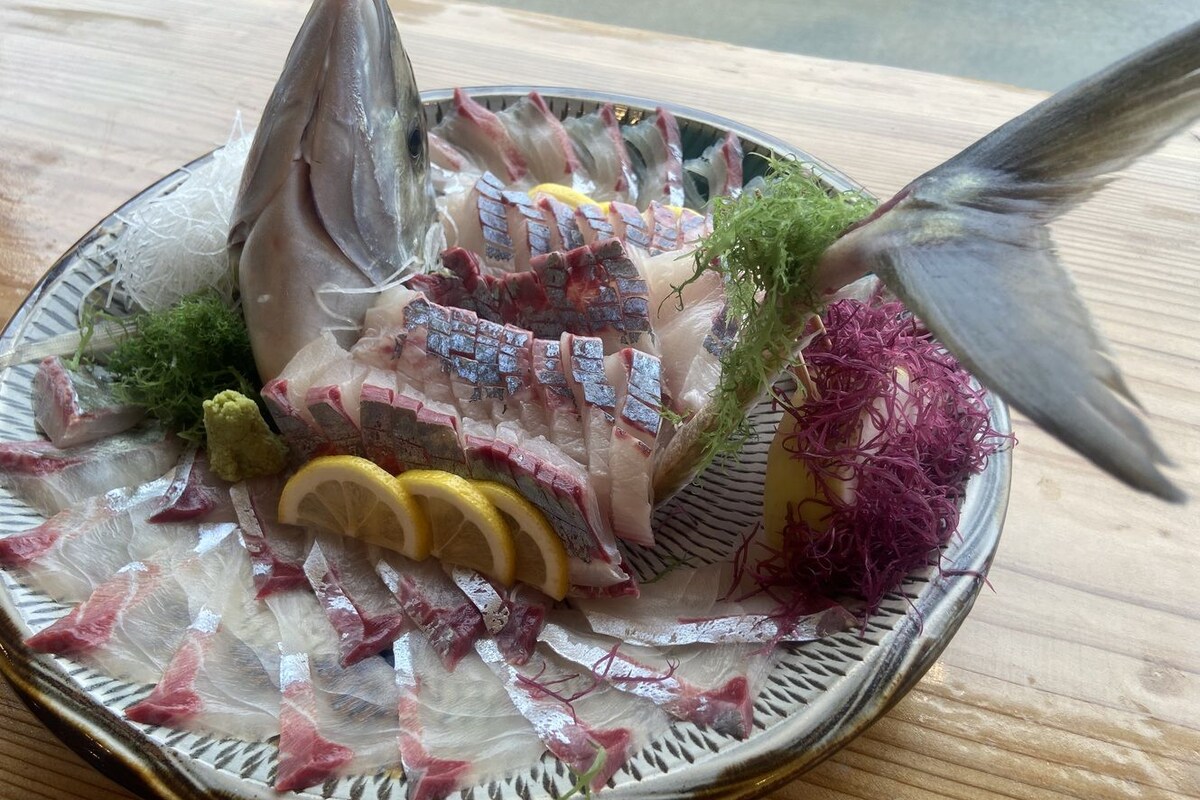 A plate of sashimi with fish, lemon, and seaweed on a wooden table.