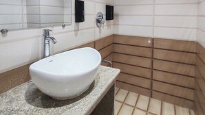A bathroom with a white sink, a mirror, a shower, and a tiled floor.