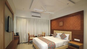 A hotel room with a bed, a desk, a chair, a TV, an air conditioning unit, and a ceiling fan.