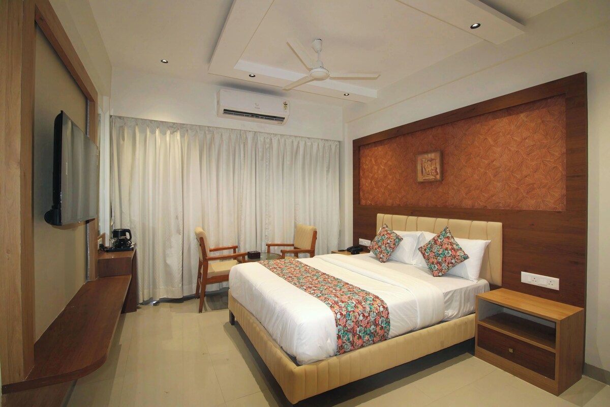 A hotel room with a bed, a desk, a chair, a TV, an air conditioning unit, and a ceiling fan.
