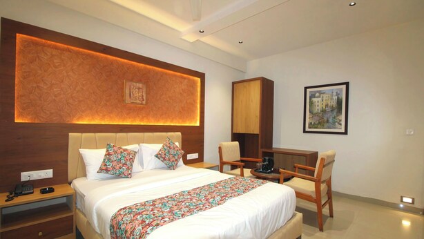 A hotel room with a large bed, bedside table, chair, desk, and artwork on the wall.
