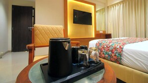 A hotel room with a bed, a television mounted on the wall, a coffee maker, and a tray with cups and a glass.