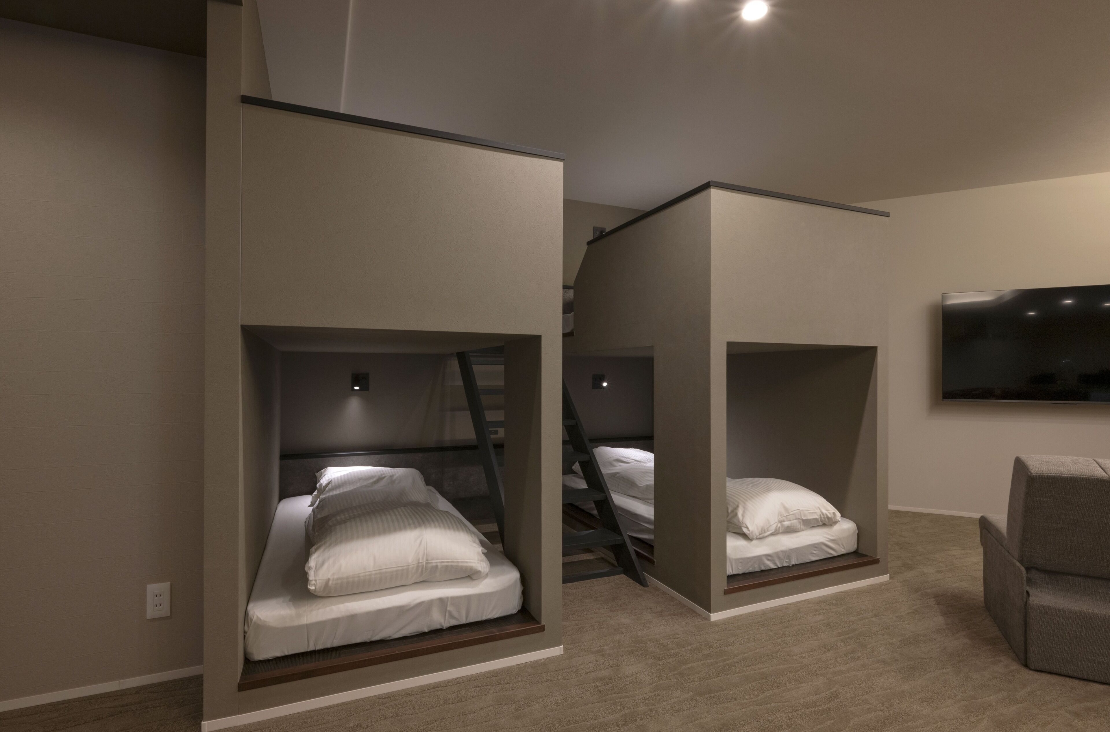A modern hotel room with bunk beds, a flat-screen TV, and a sofa.