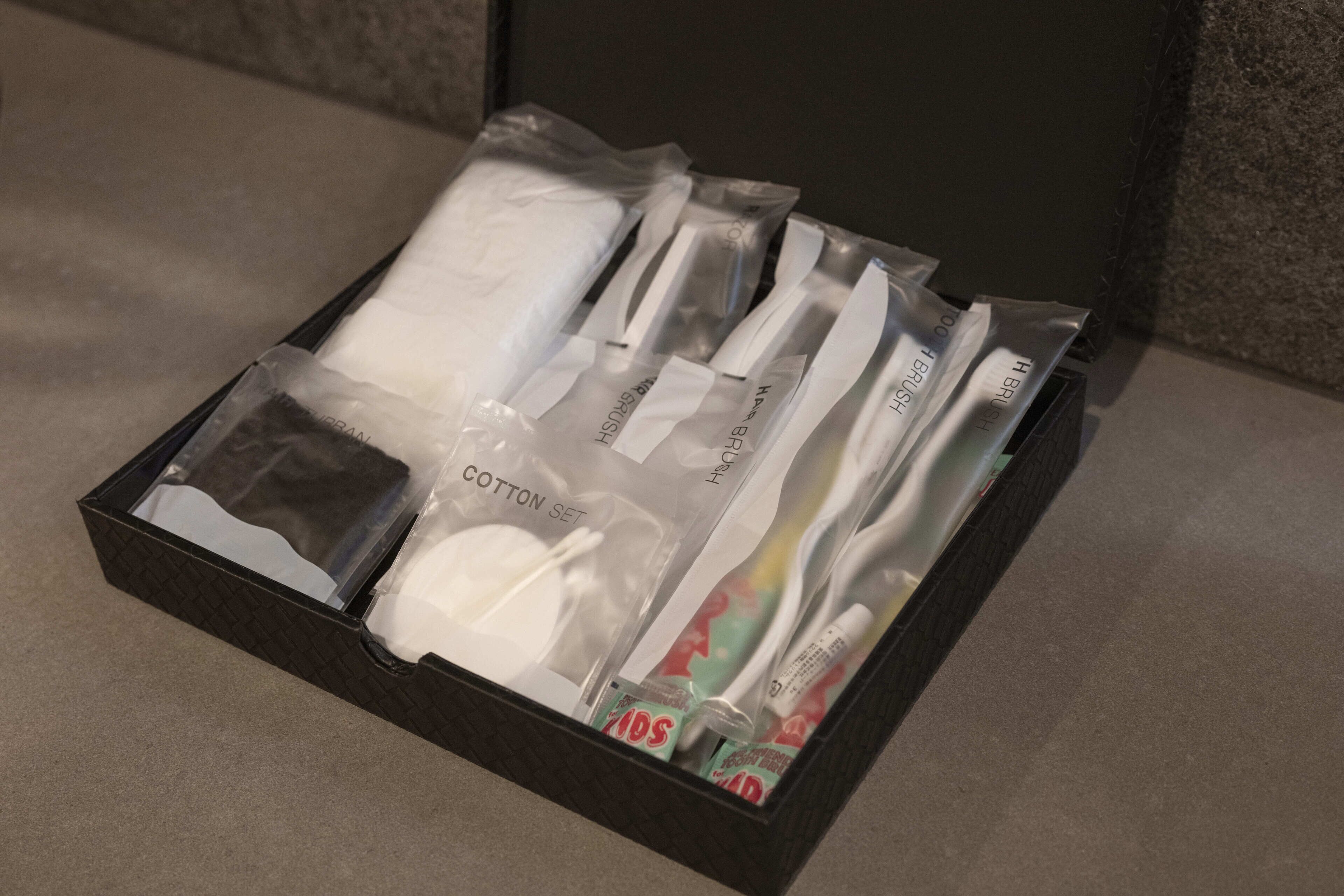 A black box containing a cotton set, a toothbrush, a tube of toothpaste, and a toothbrush head.