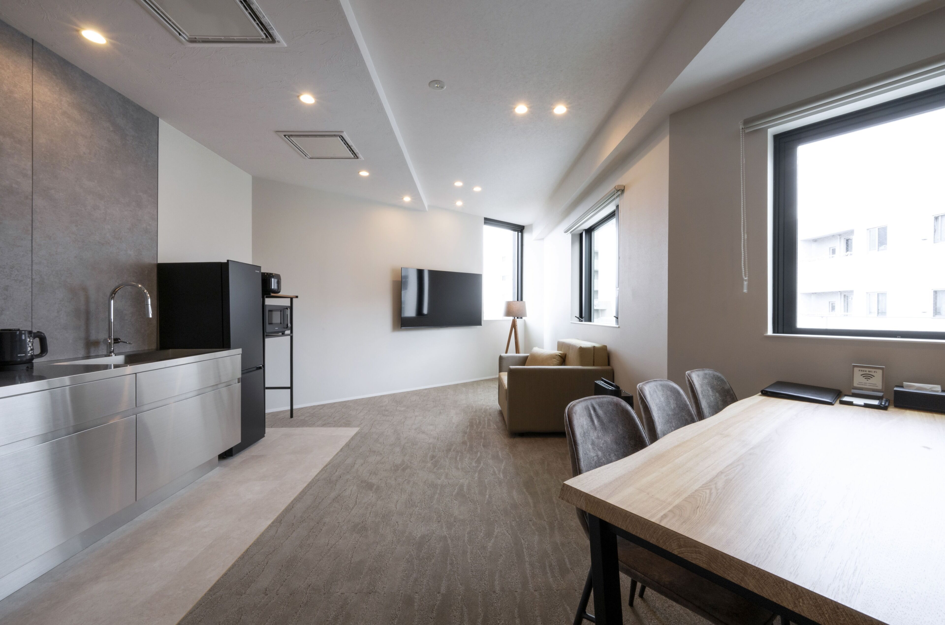 Una cocina moderna con electrodomésticos de acero inoxidable, una zona de comedor con mesa de madera y un rincón de descanso con sofá.